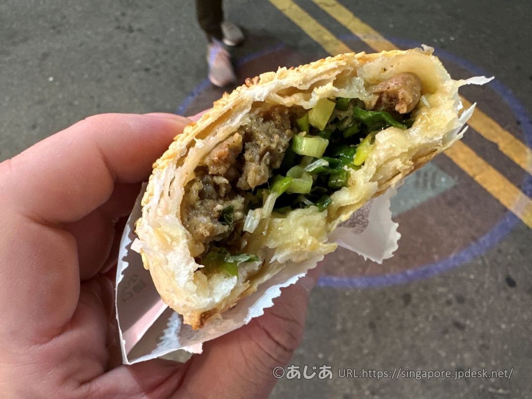 半分かじった胡椒餅の断面。何層にもなったサクサクの皮と、中のジューシーな豚肉、たっぷりの青ネギが見える