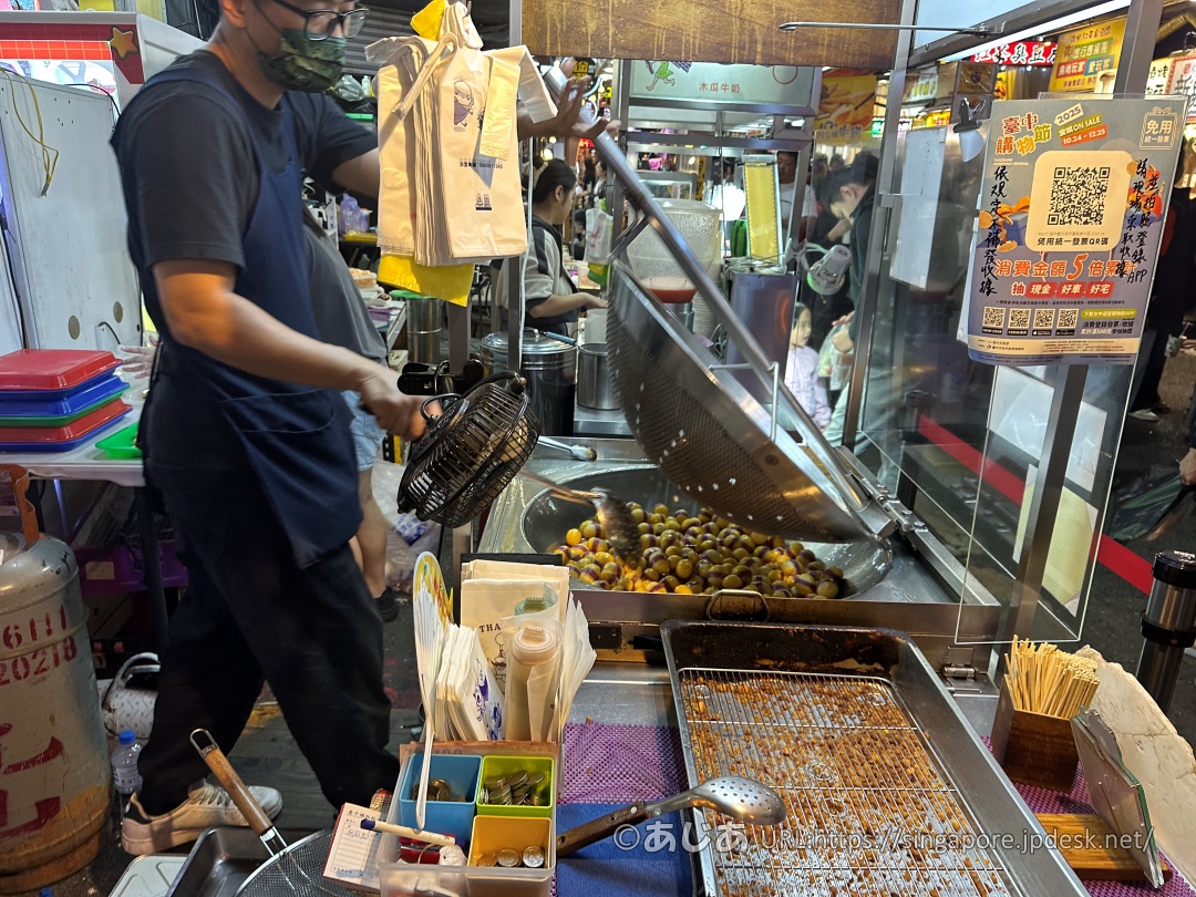 屋台のスタッフが巨大な網杓子を使って、大きな鍋の中で大量の地瓜球を油で揚げながら押し付けている様子