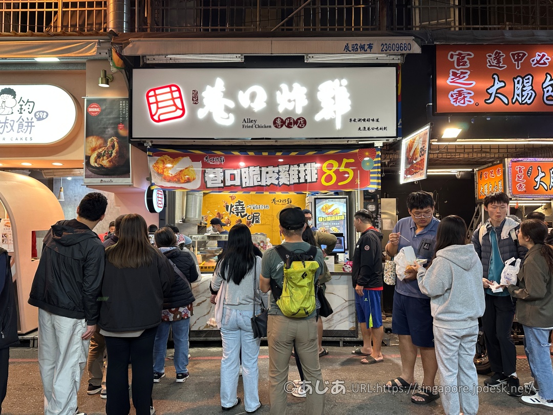 巷口炸雞の白い看板と、注文を待つ大勢のお客さんの様子