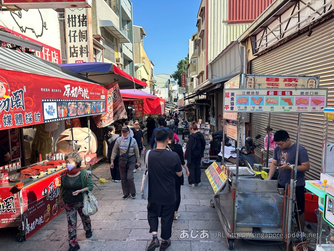 厚切り肉干(ポークジャーキー)の赤い屋台やベビーカステラの屋台の周りを歩く大勢の観光客