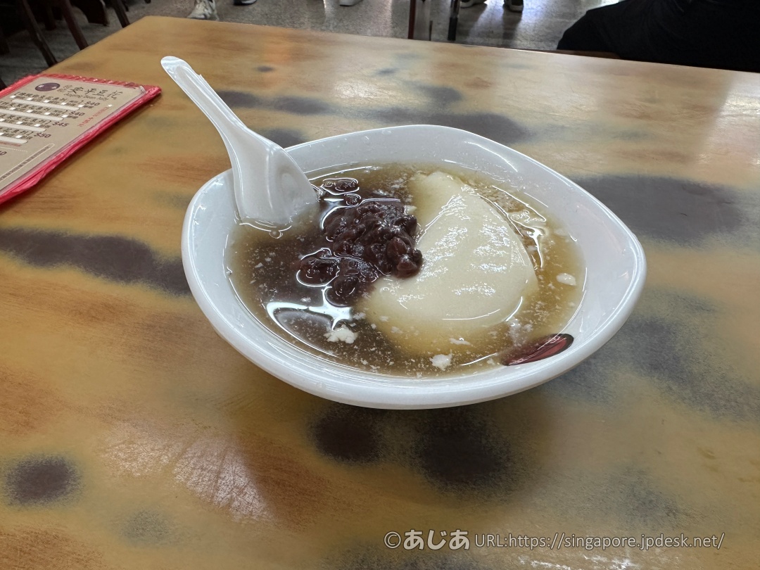 柄のあるテーブルの上に置かれた、シロップと小豆がたっぷりかかった白い豆花(トウファ)