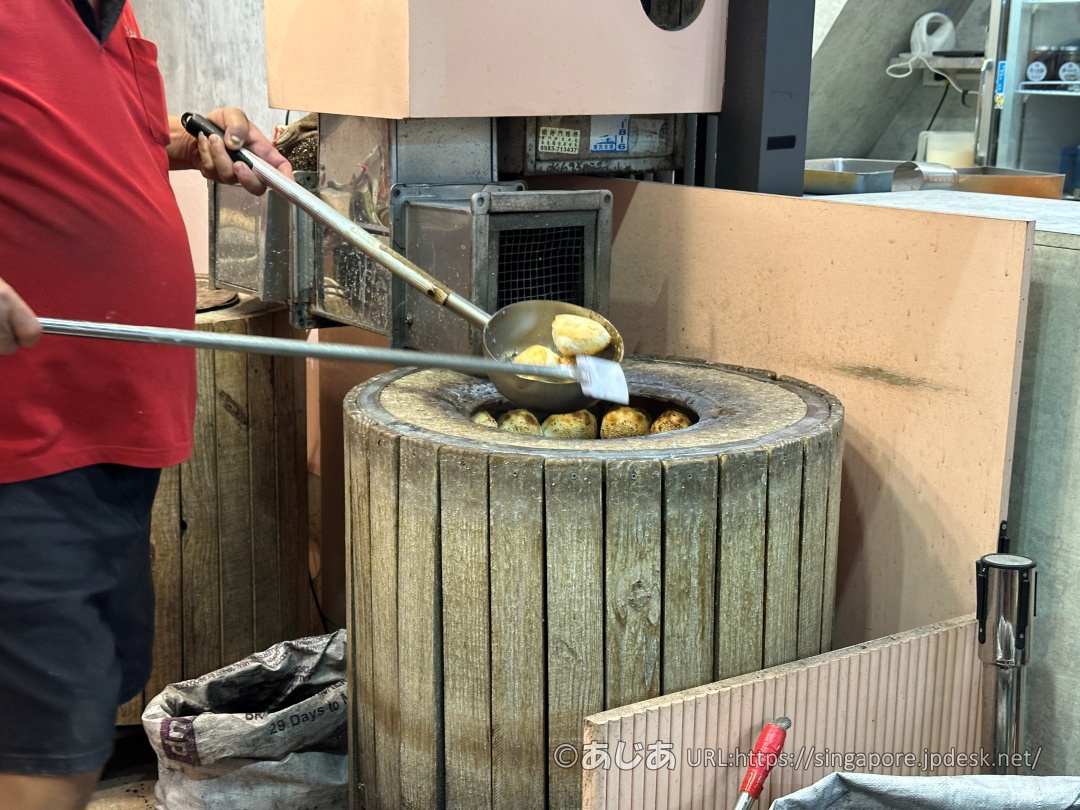 炭火窯から金属の道具を使って焼き上がった胡椒餅を取り出すスタッフ