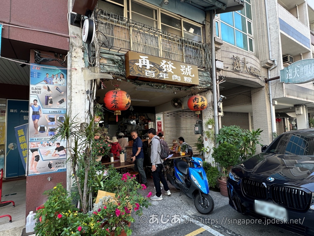 再發號百年肉粽の外観。茶色い看板と赤い提灯が特徴的で、お店の前に人が集まっている様子