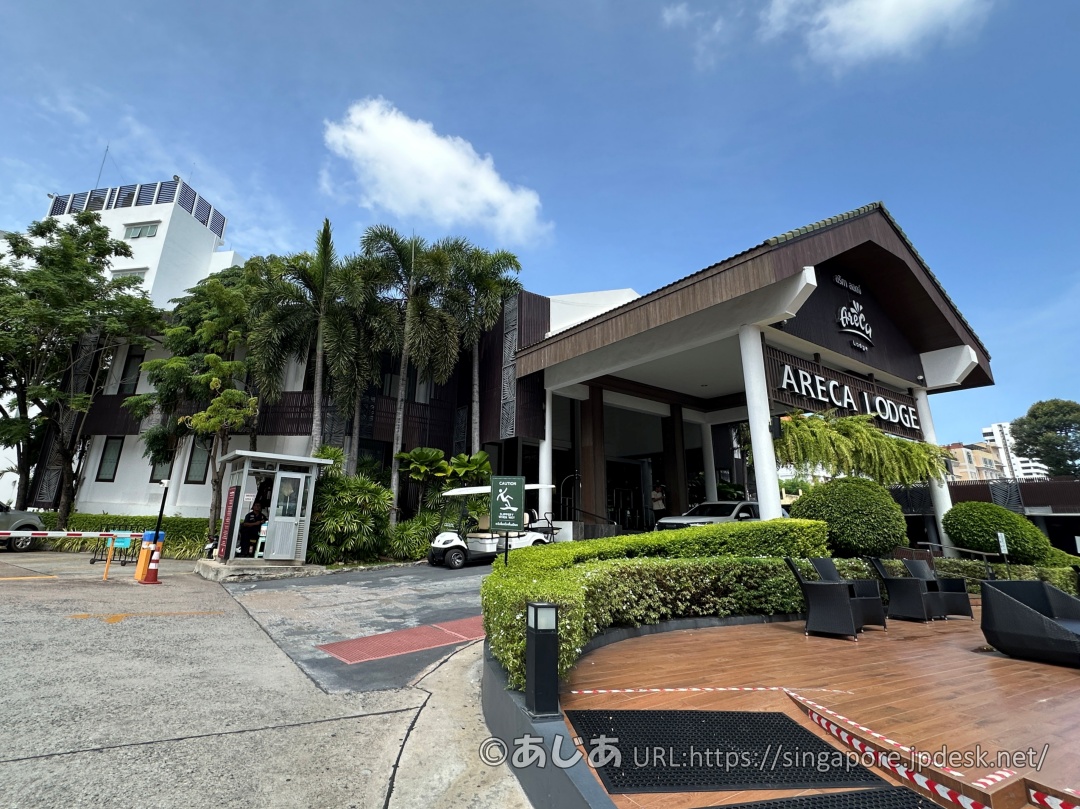 青空の下に建つアレカロッジの外観。ヤシの木とARECA LODGEの看板が見える。