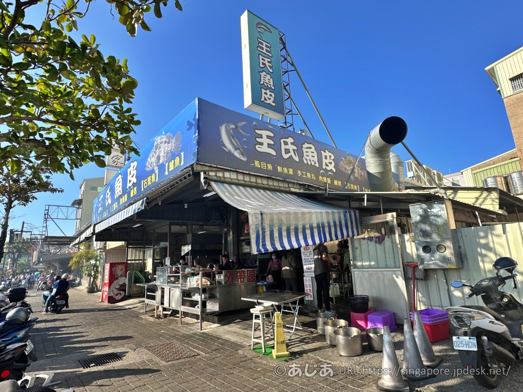 大きな青い看板を掲げた王氏魚皮の外観。お店の前にバイクが並び、賑わっている様子