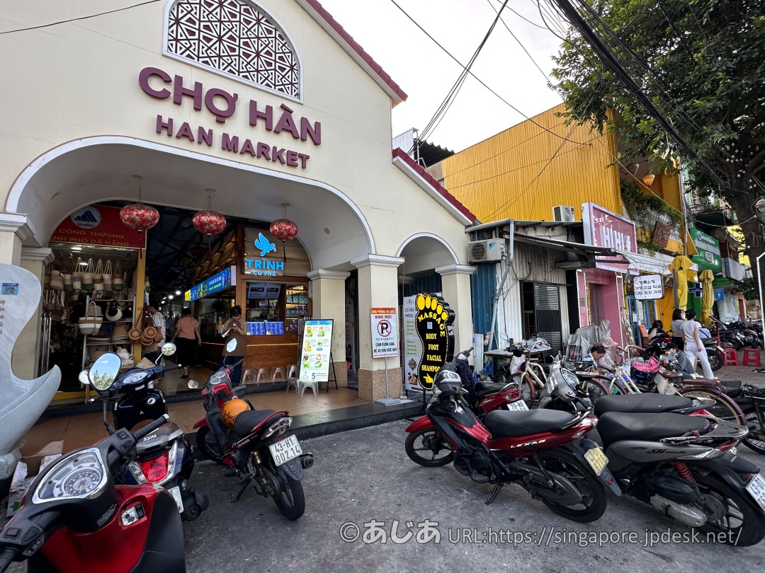 HAN MARKET（ハン市場）のアーケード入り口。そのすぐ左側に青い鳥のロゴが目印のカフェ「TRỊNH CÀ PHÊ」がある。店前にはたくさんのバイクが停まっている。