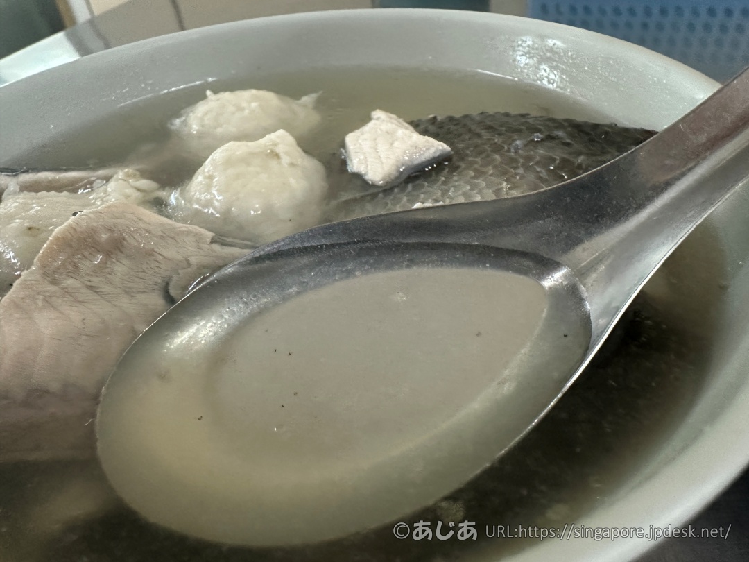 レンゲですくった、透明でほんのり黄金色をした魚のスープのアップ