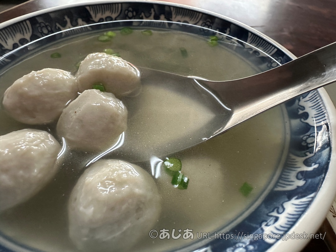 レンゲですくった大きな白い魚丸（つみれ）と透明なスープのアップ