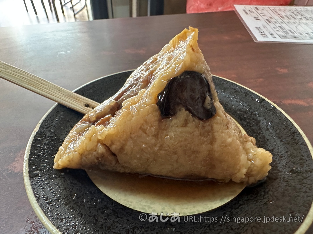 黒っぽいお皿に乗った、タレのかかった定番の肉粽（ちまき）