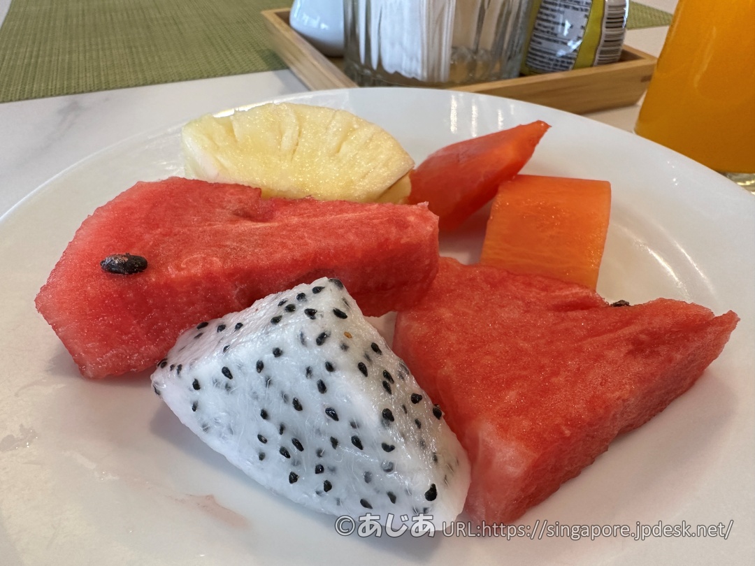 お皿に盛られたカットフルーツ（スイカ、パイナップル、パパイヤ、白肉のドラゴンフルーツ）。