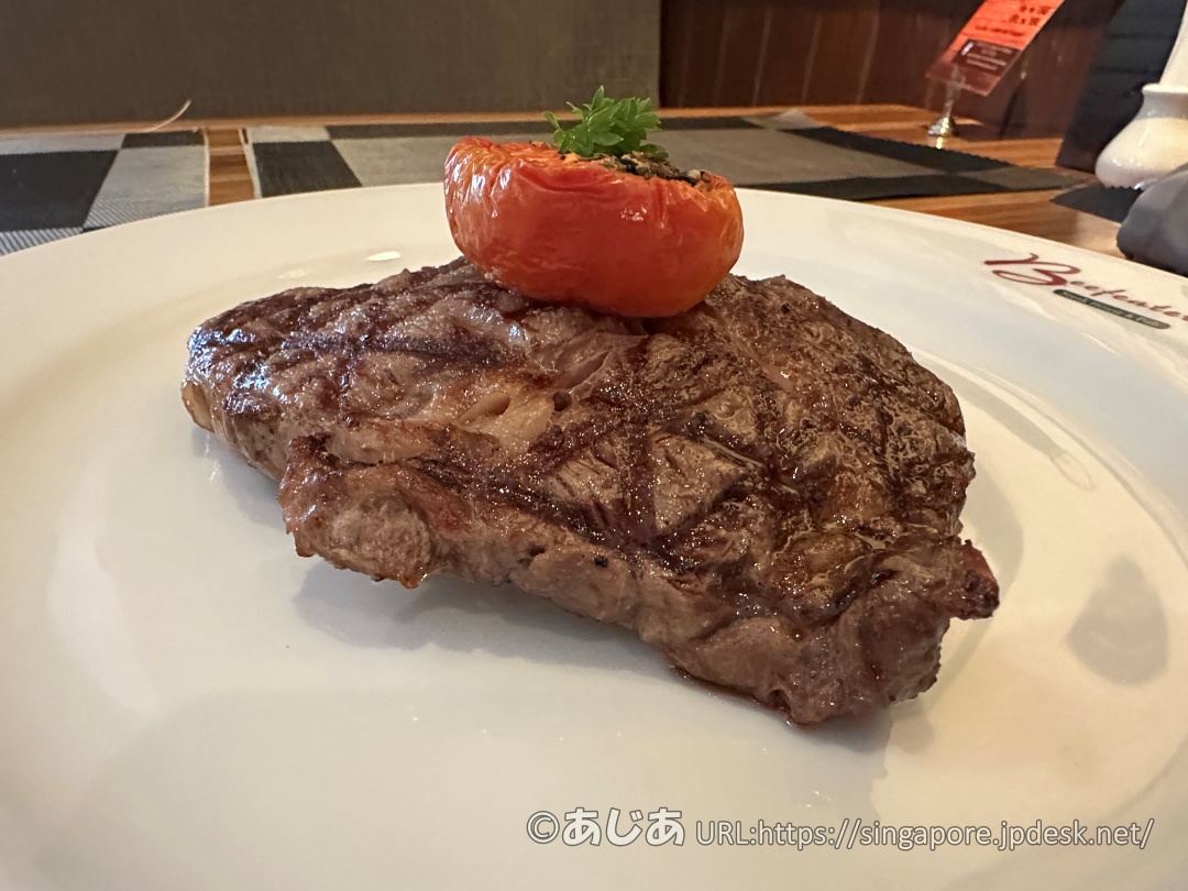 リブアイステーキのアップ写真。表面に綺麗な網目状の焼き目がついており、上にローストされたトマトが乗っている。