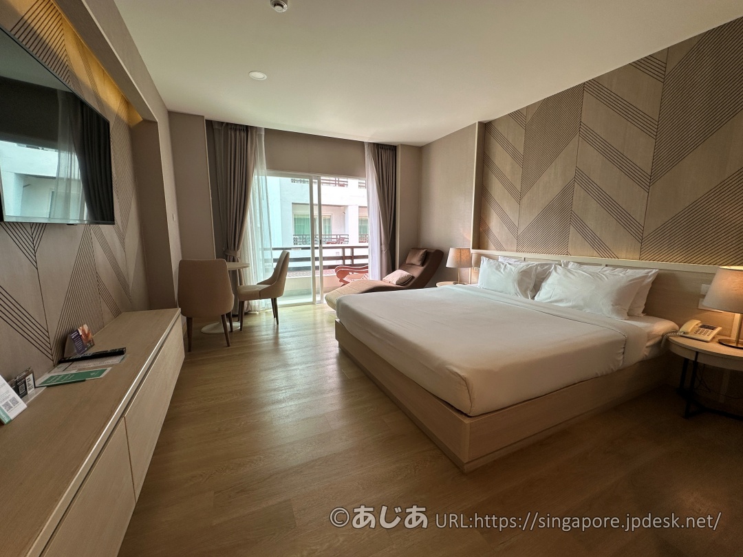 アレカロッジのスタンダードプラスルーム内観。キングサイズのベッド、テレビ、窓際の椅子とテーブル、リラックスチェアが見える。
