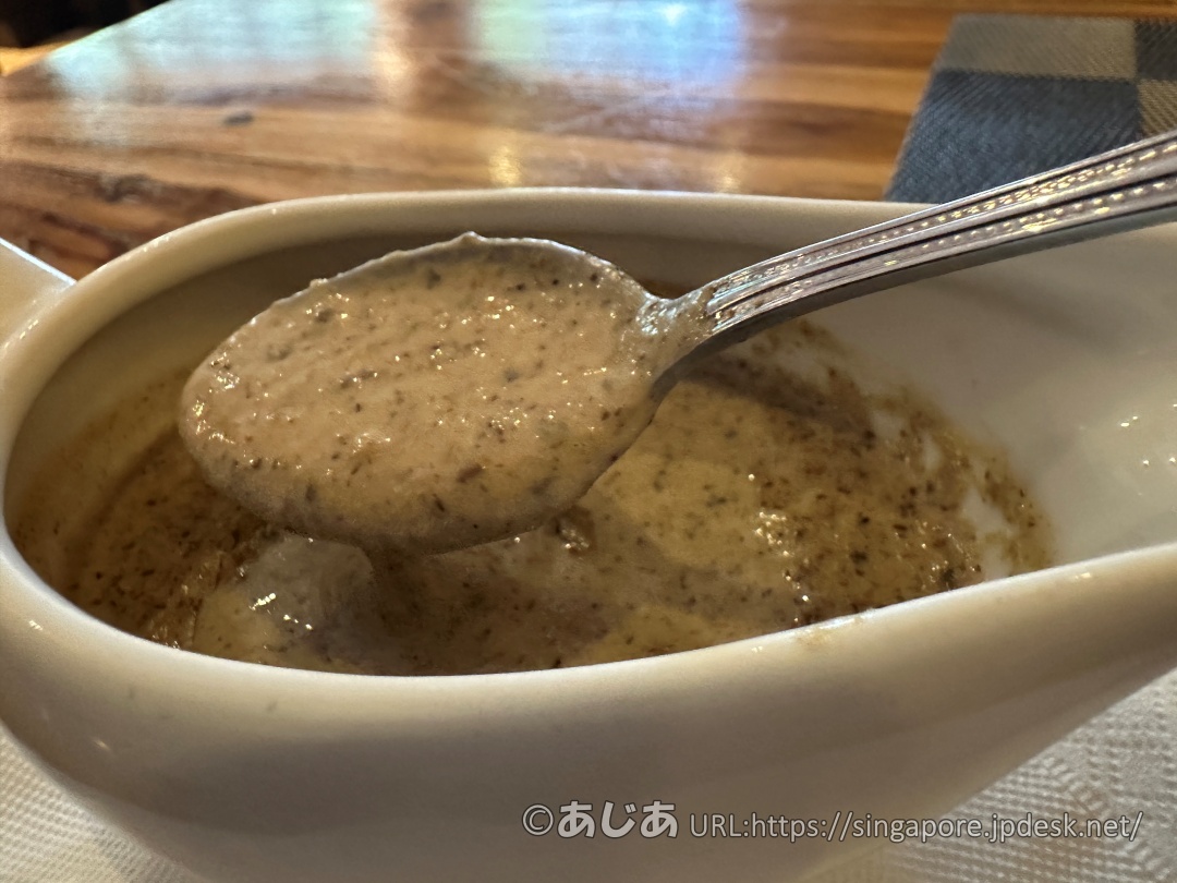 ソースポットに入ったマッシュルームソースをスプーンですくい上げている様子。クリーミーでキノコの粒がたくさん見える。