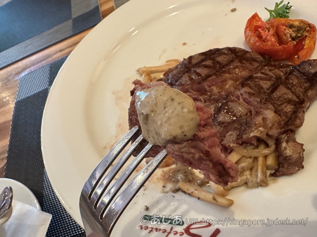 マッシュルームソースをたっぷりかけたステーキの一切れをフォークで持ち上げている様子。お肉の下には付け合わせのキノコ炒めが見える。