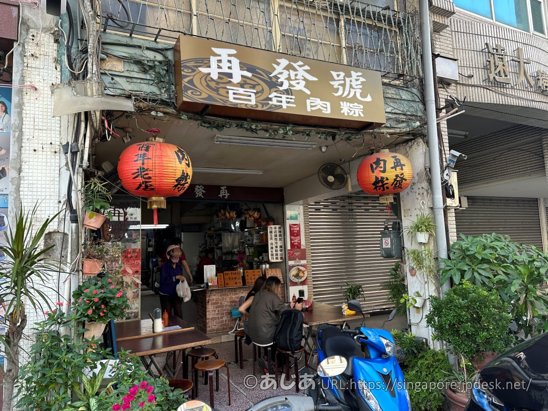 再發號百年肉粽の店頭のアップ。赤い提灯と、店先のテーブルに座るお客さんたち