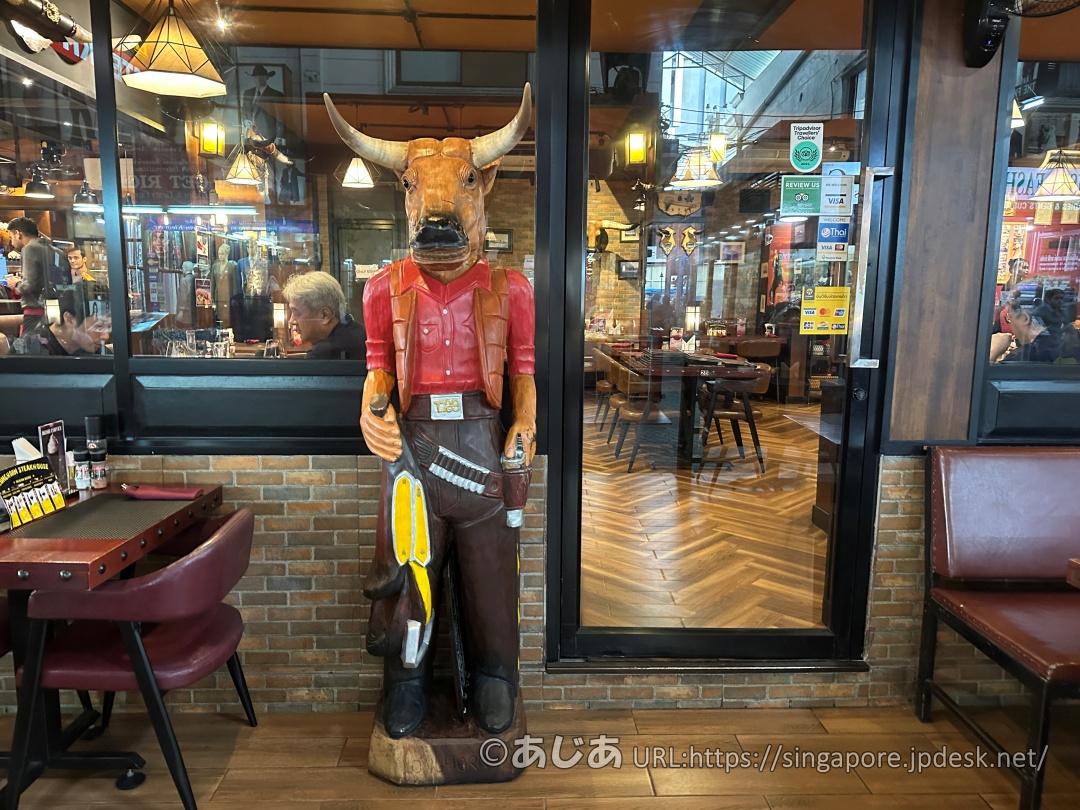 ガンベルトを巻き、ウエスタンシャツを着た牛の顔を持つ木彫り人形が入り口に立っている。