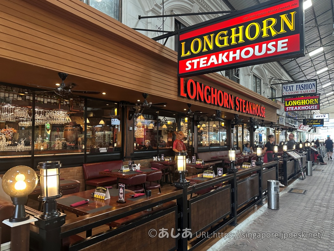 アーケード内にあるロングホーンステーキハウスの店舗外観。テラス席が並び、大きな赤と黄色の看板が出ている。