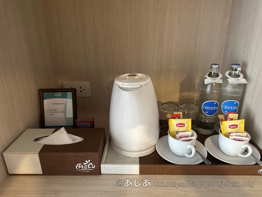 白い電気ケトル、瓶入りのクリスタルウォーター2本、マグカップとティーバッグ類がセットされたミニバー。