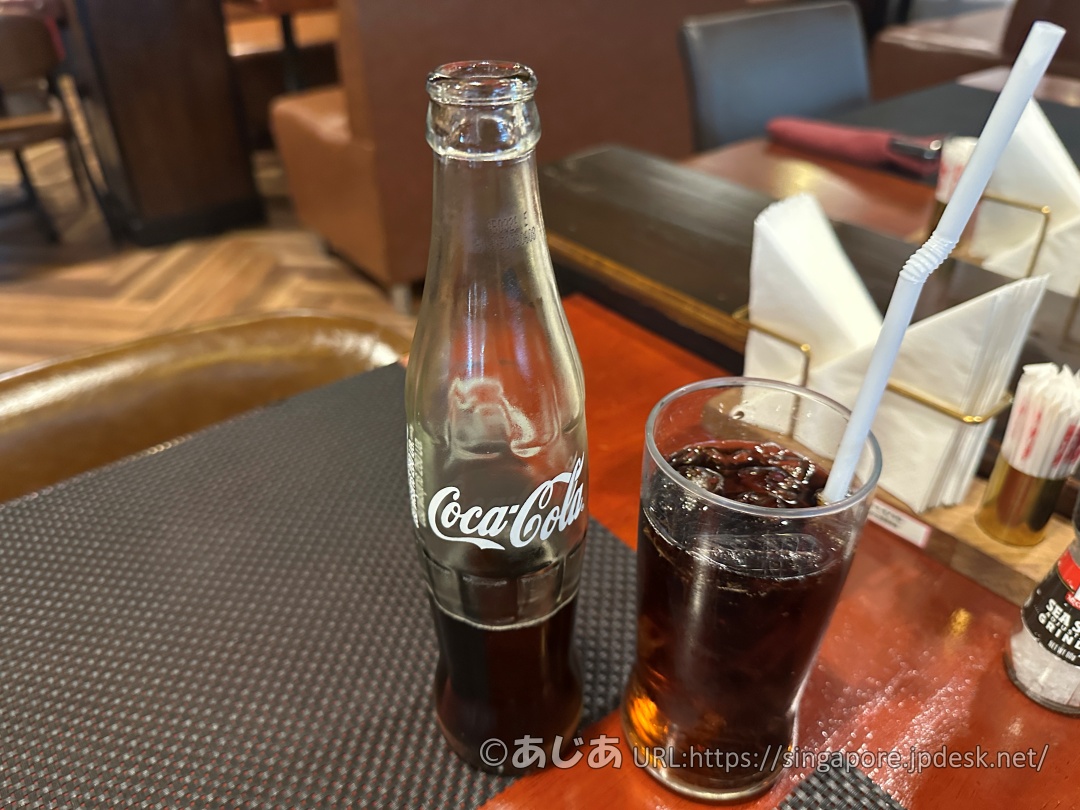 テーブルの上のランチョンマットに置かれた瓶入りのコカ・コーラと、氷が入ったグラス。