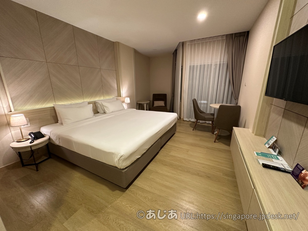 フローリングの床にキングベッド、窓際にテーブルセットとリラックスチェアが配置された、別日のスタンダードプラスルーム全体の内観。