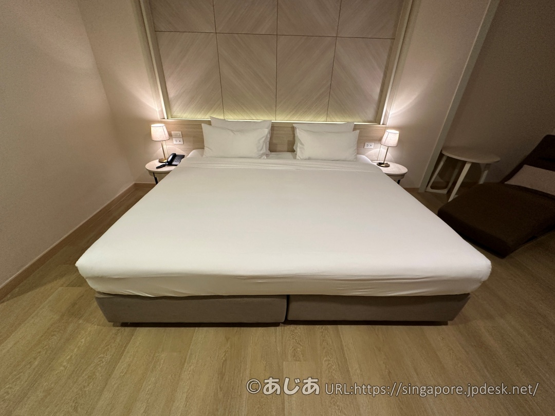 正面から撮影したアレカロッジの大きなキングベッド。真っ白なシーツと幾何学模様の木製ヘッドボードが特徴的。