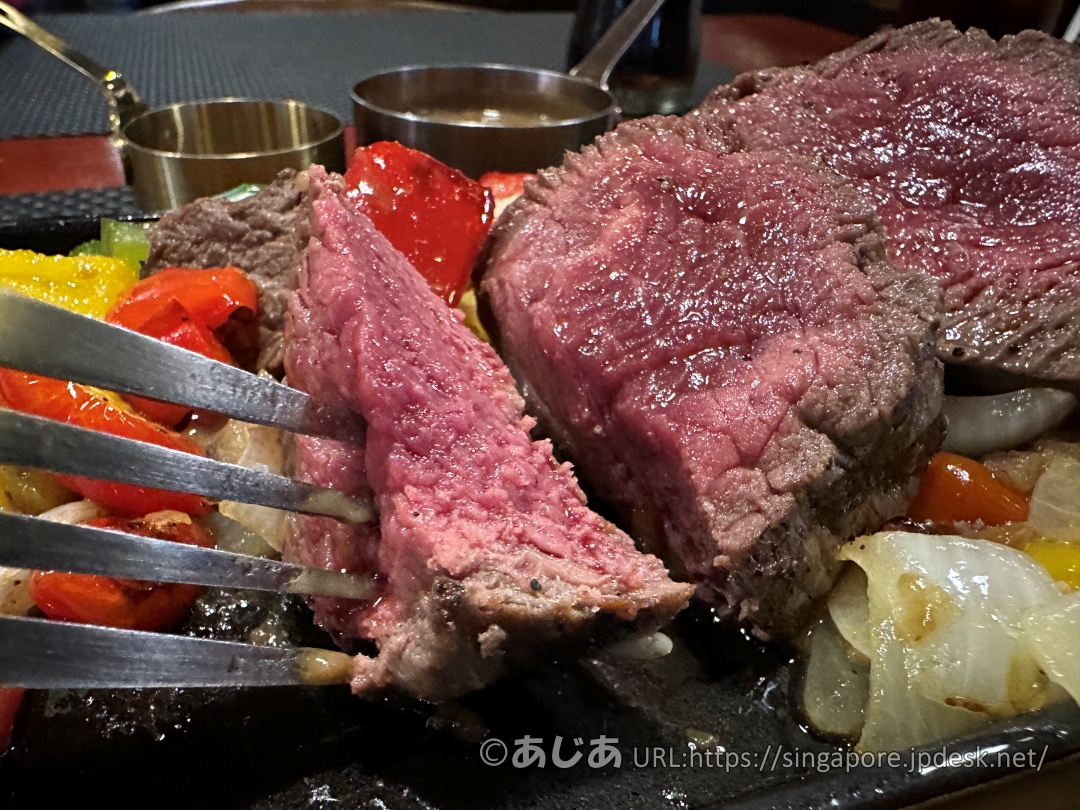 フォークとナイフでカットされたステーキの断面のアップ写真。見事なレア〜ミディアムレアの美しい赤身肉で、肉汁が滲み出ている。