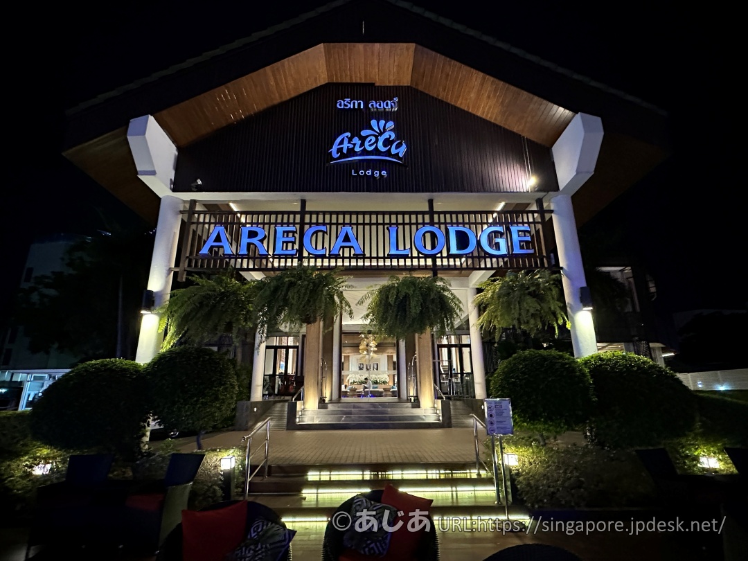 夜間にライトアップされたアレカロッジのエントランス。ARECA LODGEの青いネオンが光っている。