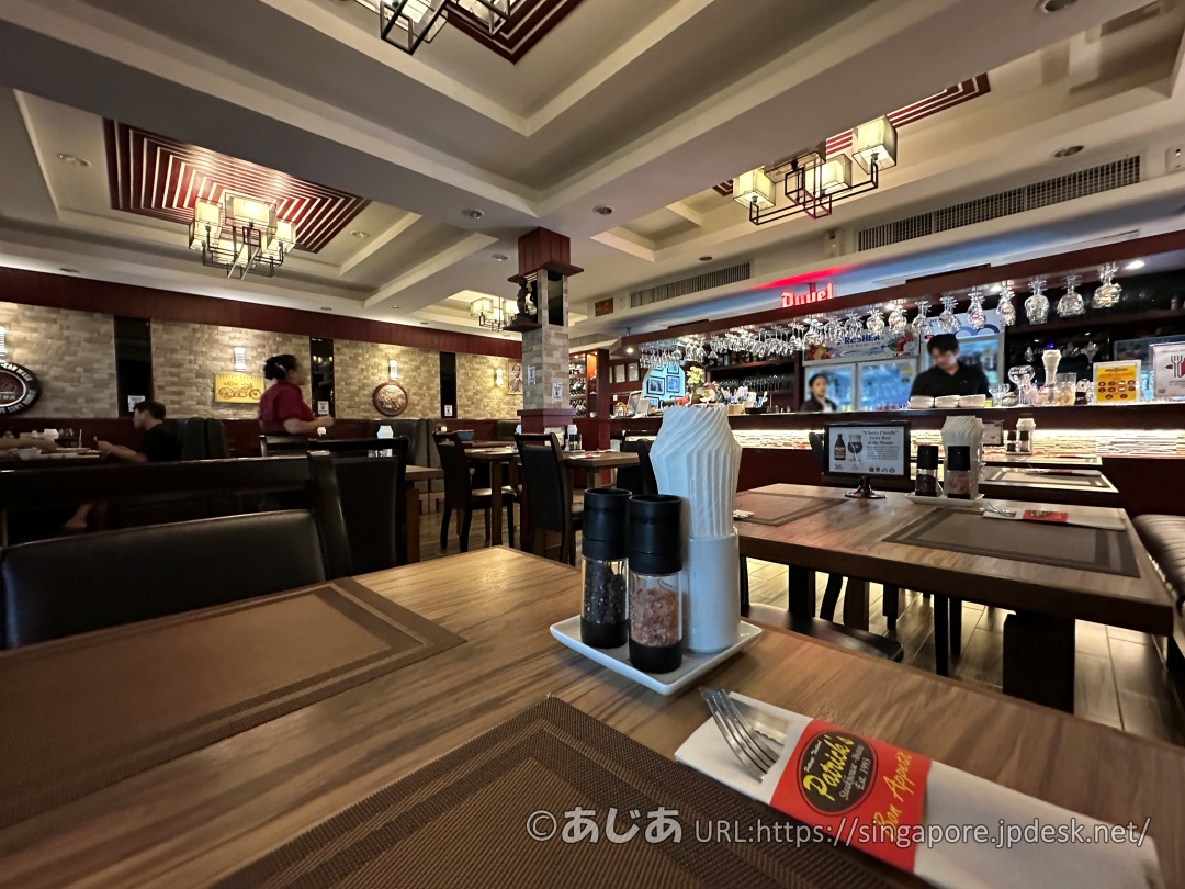 パトリックスの店内。上品な照明と木目調のテーブル、奥にはグラスが吊るされたバーカウンターが見える。