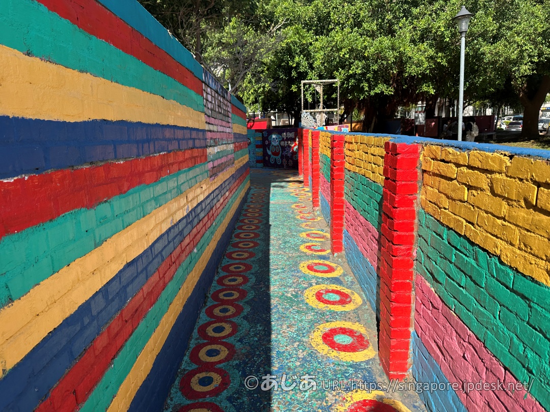 赤、青、黄、緑などで横縞に塗られたレンガの壁と、模様が描かれた細い路地。