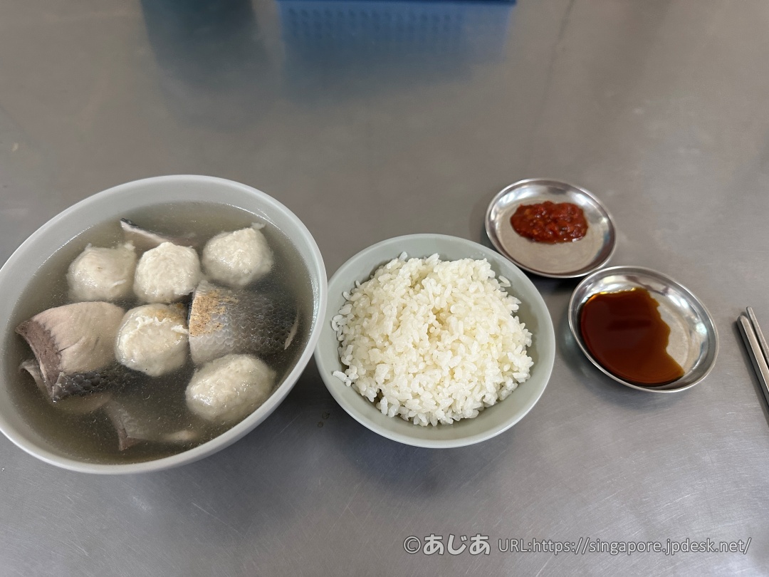 テーブルに置かれた魚皮と魚のつみれが入った透明なスープ、お茶碗一杯の白ご飯、そして小皿に入ったとろみ醤油と辛味調味料