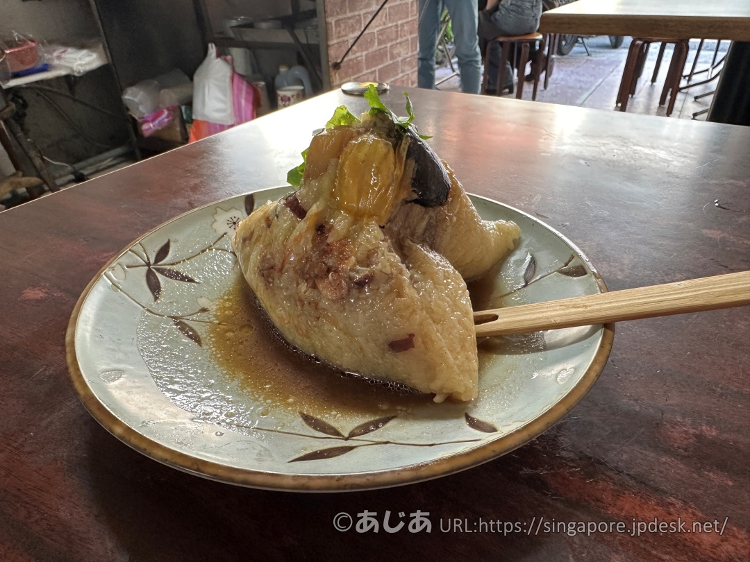 特製八寶肉粽の全体写真。お皿に乗った特大サイズのちまきにタレがかかっている