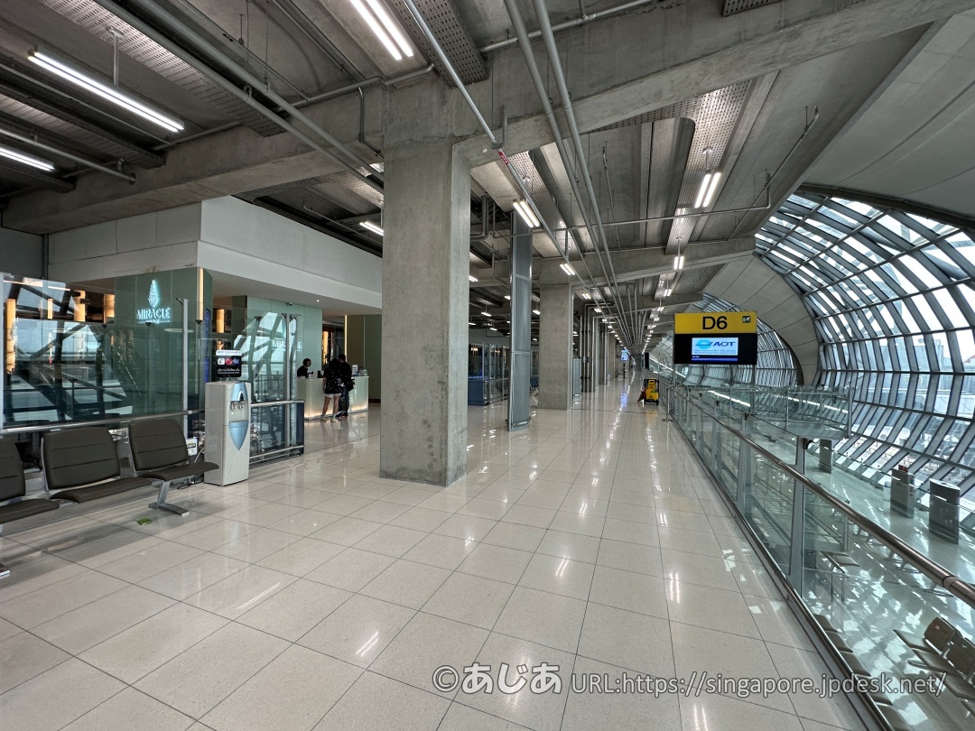 ガラス張りの巨大なターミナル通路と、左側に見えるMiracle Loungeの外観。D6ゲートの案内板がある。