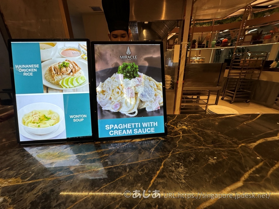 ライブキッチンのカウンターに置かれたデジタルメニュー。HAINANESE CHICKEN RICE、WONTON SOUP、SPAGHETTI WITH CREAM SAUCEの3種類が表示されている。