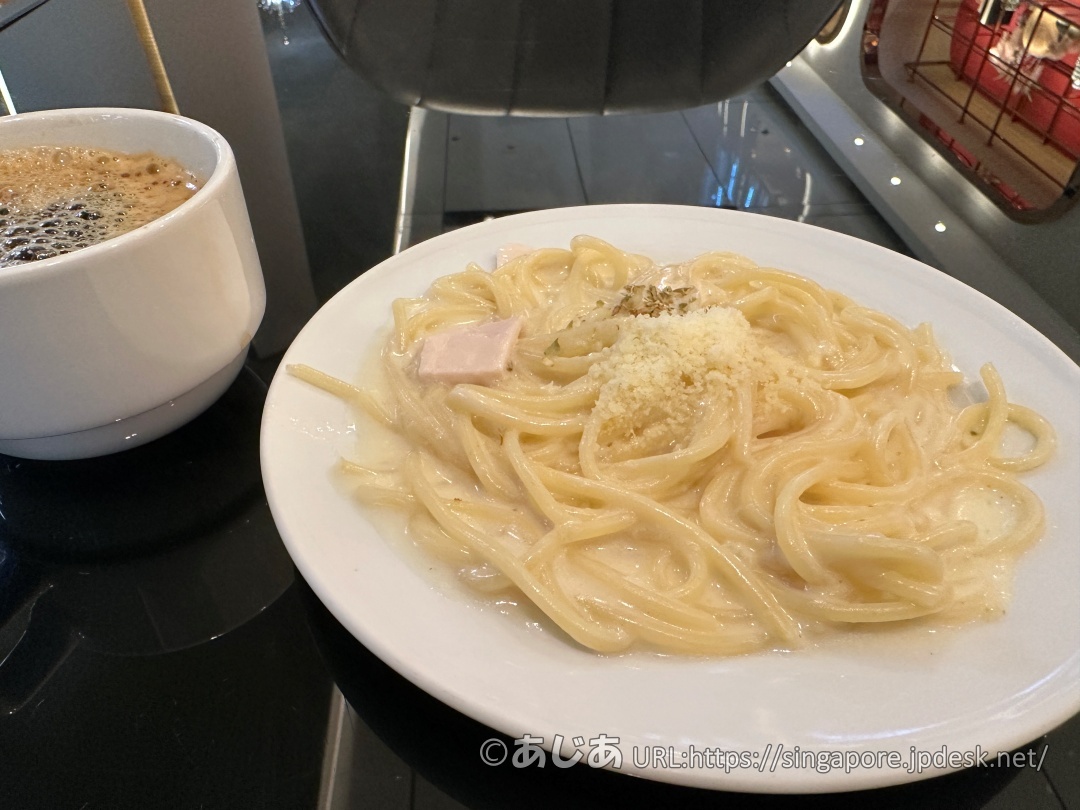 お皿に盛られたクリームソースのスパゲッティ。粉チーズがかかっており、左側にコーヒーカップがある。