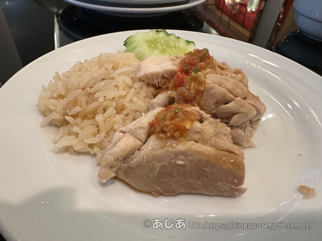 お皿に盛られたチキンライス。鶏肉の上に特製のタレがかかっており、奥にキュウリが添えられている。