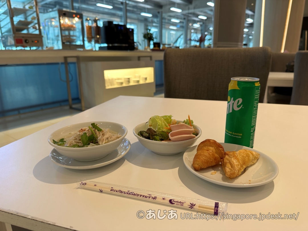 白いテーブルに並べられたスープ麺、サラダ、クロワッサン類、スプライトの缶。手前にはお箸が置かれている。