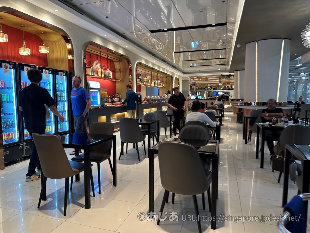 黒いテーブルとグレーの椅子が並ぶダイニングエリア。左側には青く光るドリンク冷蔵庫が見える。