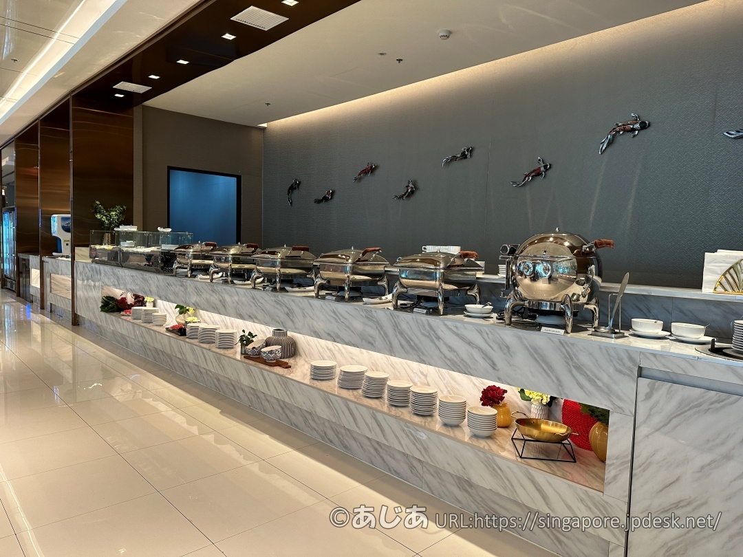 壁に鯉のオブジェが飾られた、大理石調の長いビュッフェカウンター。銀色の保温器が多数並んでいる。