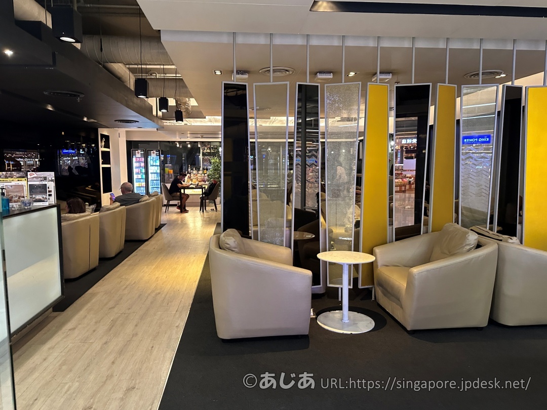 黄色と鏡面のパーテーションで仕切られたラウンジ内。ベージュの1人掛けソファーと丸いテーブルが配置されている。