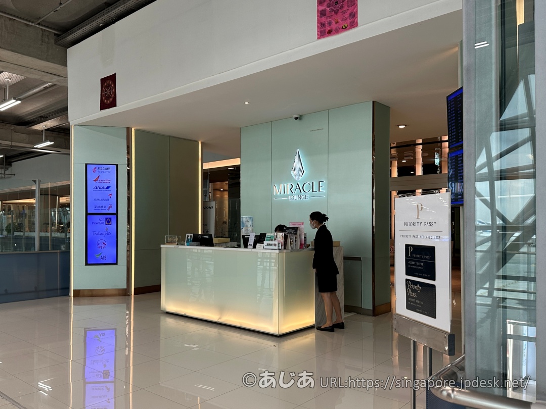 ライトグリーンの壁にMIRACLE LOUNGEのロゴが光る受付。手前にプライオリティパスの案内板がある。