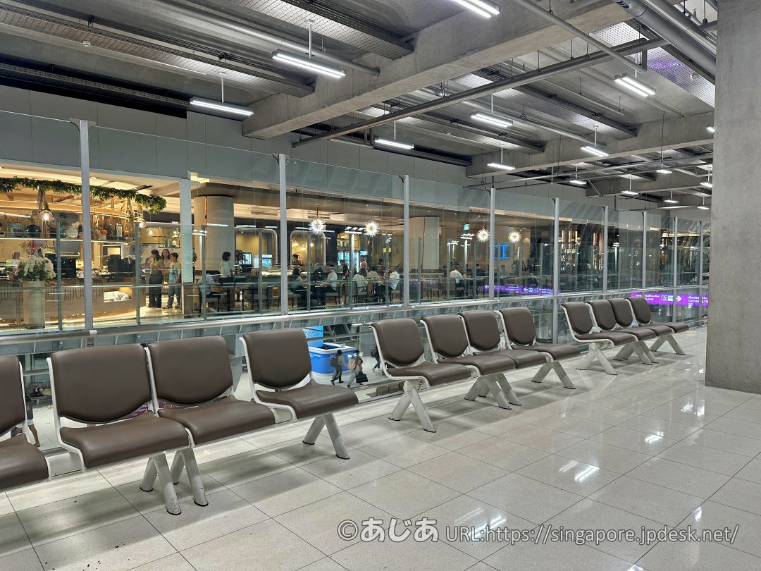 コンコース通路に並ぶ待合用のベンチと、その後ろのガラス越しに見えるラウンジ内の様子。