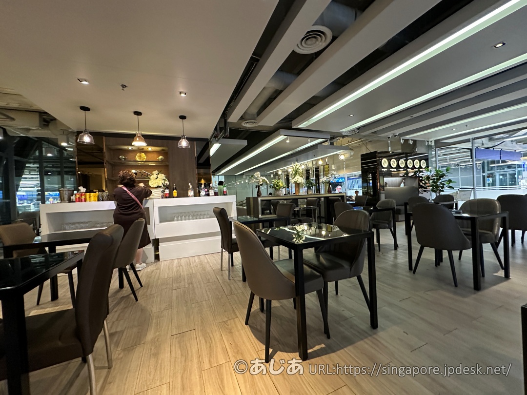 黒いテーブルとグレーの椅子が並ぶラウンジ内部。奥にはドリンクが並ぶバーカウンターがある。