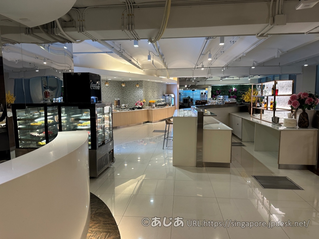 白い床と白い曲線的なカウンターがあるラウンジのダイニングエリア。左側にケーキなどが入った冷蔵ケースが見える。