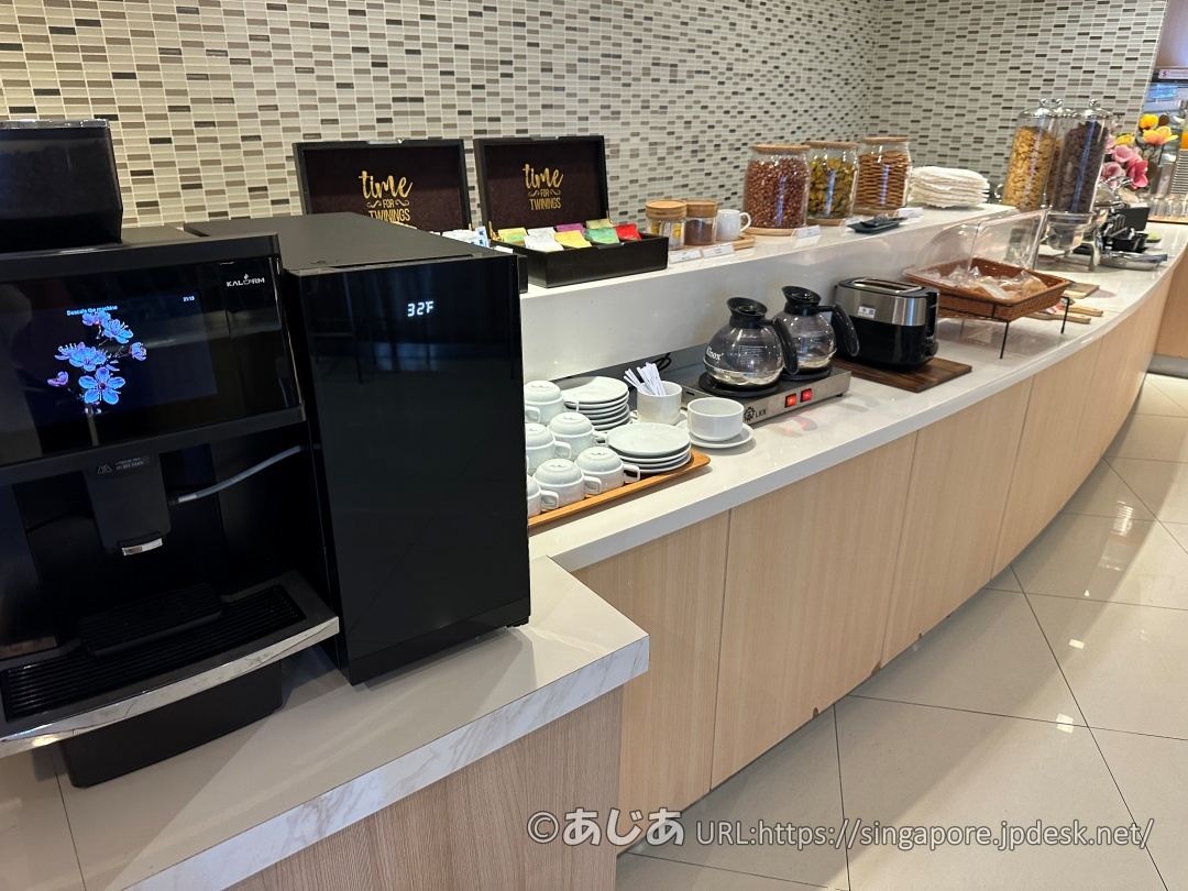 白いカウンターの上に置かれた黒いエスプレッソマシンと、カップ&ソーサー、奥にはトワイニングの紅茶ボックスが並んでいる。