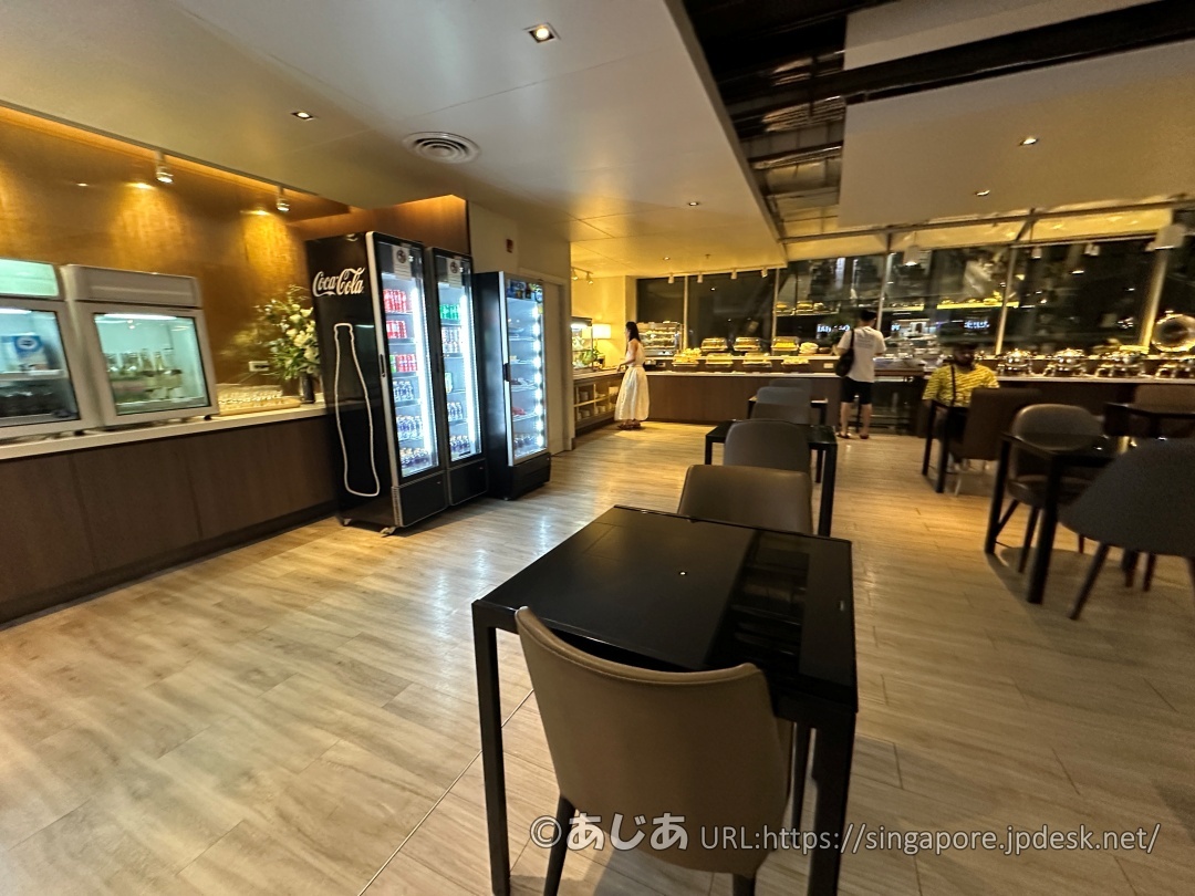 黒いテーブルが並ぶダイニングエリア。奥の壁沿いにドリンク用の冷蔵庫やビュッフェ台が設置されている。