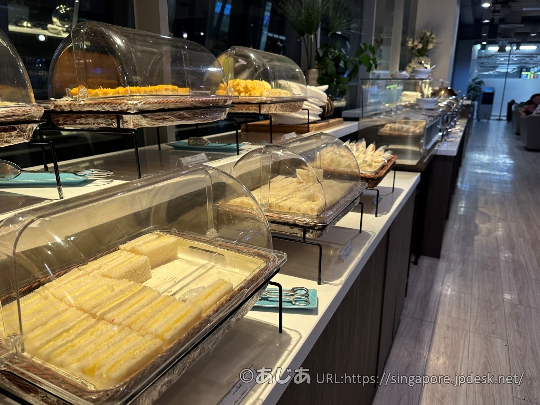 白いカウンターの上に、透明なカバー付きの容器に入れられたサンドイッチやケーキなどの軽食が並んでいる。