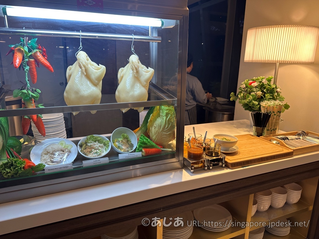 ガラスケースの中に丸ごとの茹で鶏が吊るされているカウンター。手前にはカオマンガイのサンプルや、数種類のタレが用意されている。