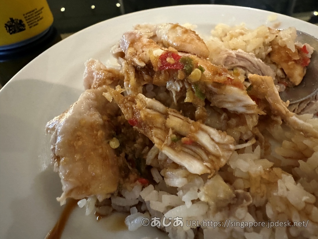 チキンライスのアップ写真。鶏肉の上に、刻んだ唐辛子などが入った特製のタレがたっぷりとかかっている。