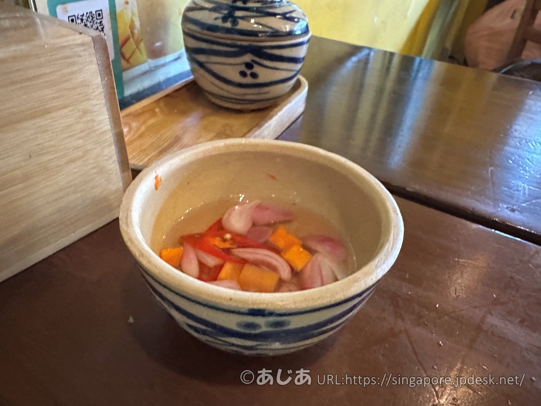 テーブルの上に置かれた小さな陶器の器。中にはスライスされた赤玉ねぎ、唐辛子、ニンジンが甘酢に漬かっている。