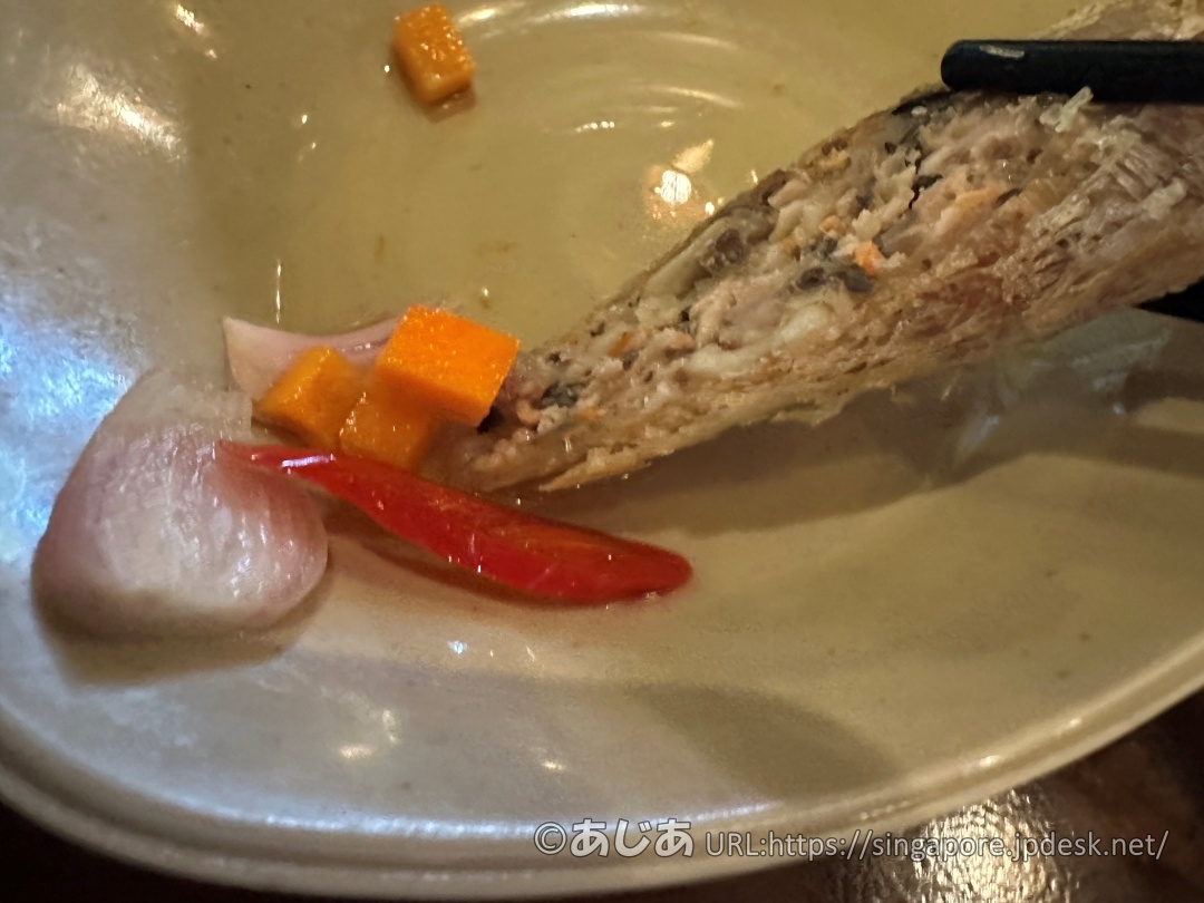 お箸で持った揚げ春巻きに、甘酢漬けの玉ねぎと唐辛子、ニンジンを乗せているところのアップ写真。